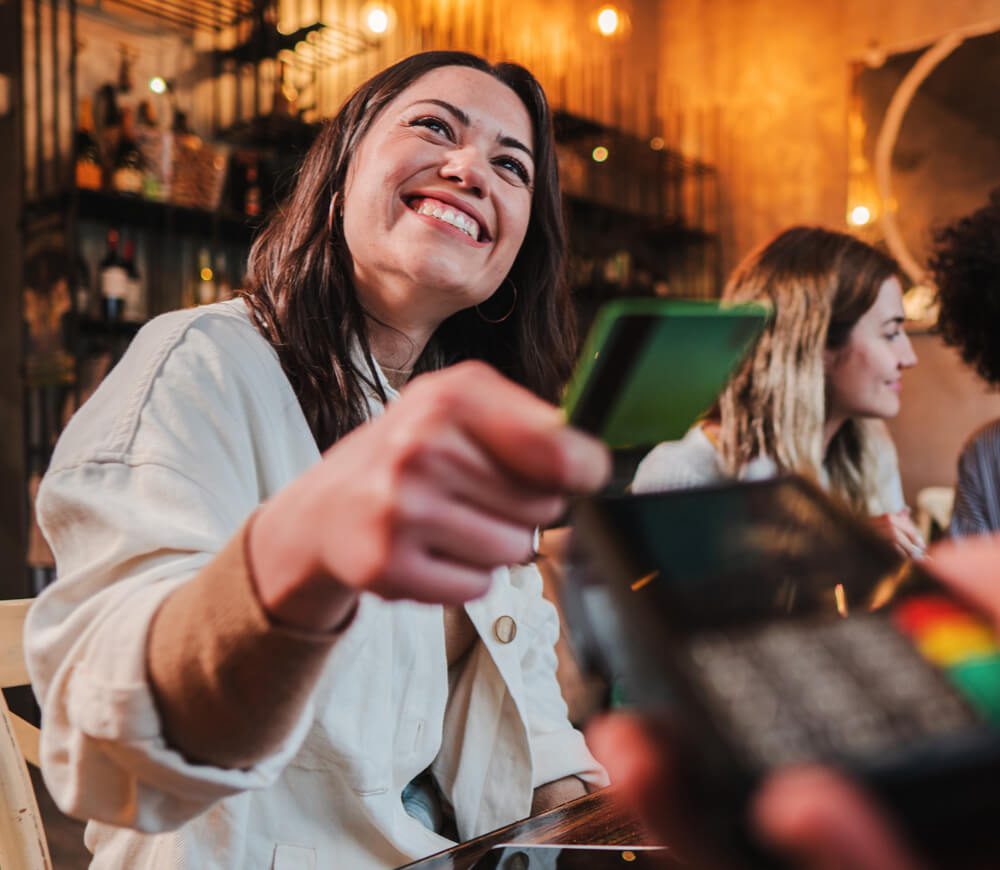 A young woman is smiling while handing over her debit card at a restaurant.